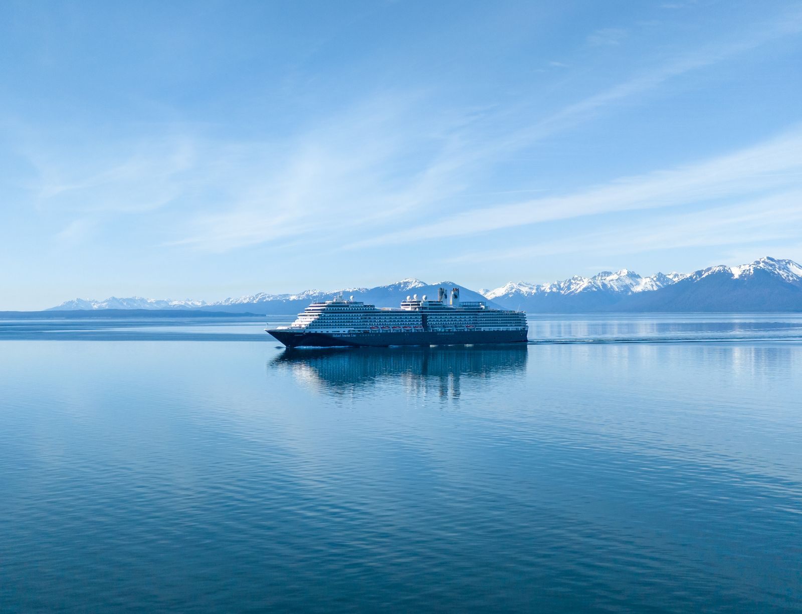 Cruise ship on calm water below snowcapped Alaska mountains, the kind of trip cruise discounts can make affordable