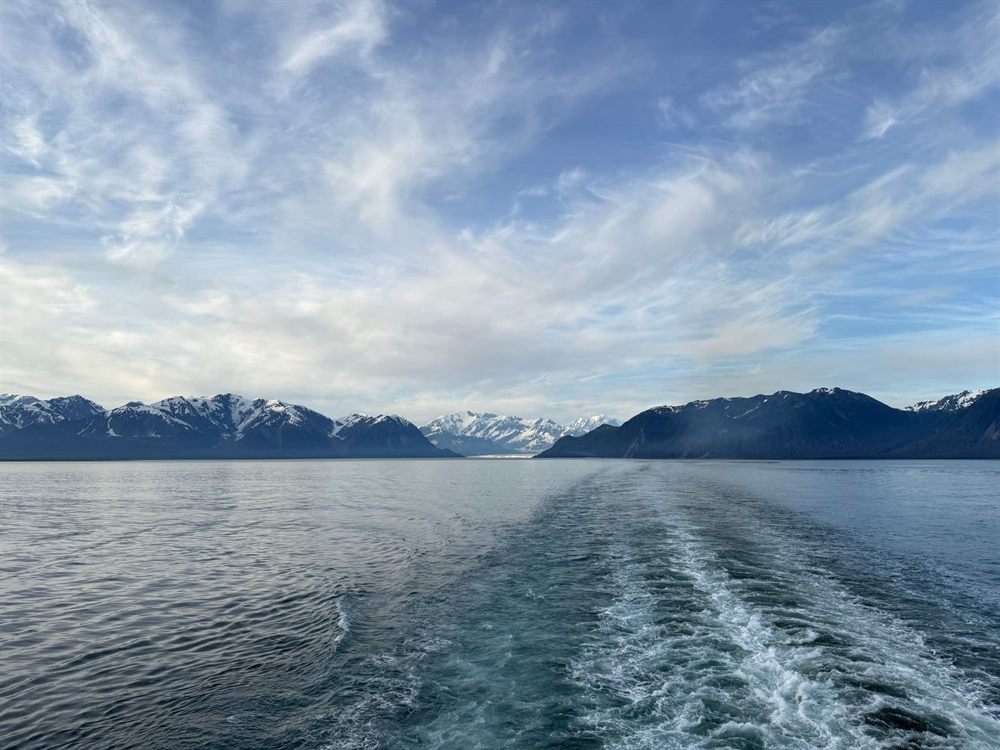 Ship wake trailing across calm water toward distant mountains