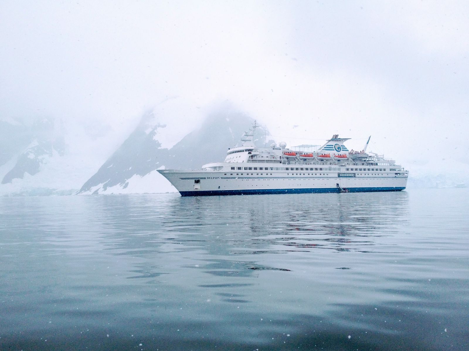 Expedition cruise ship sailing through still, misty Antarctic waters